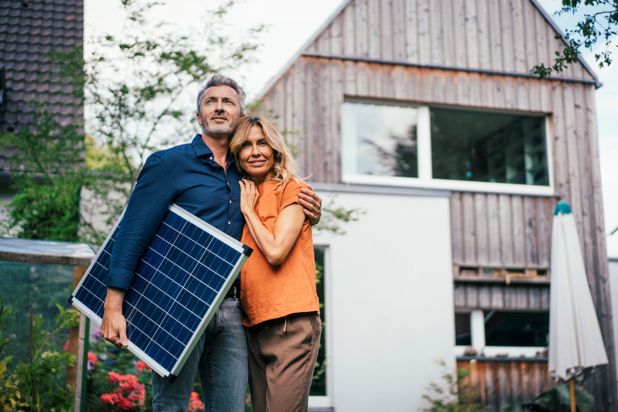 PIA Paar steht mit Solarplatte vor Haus