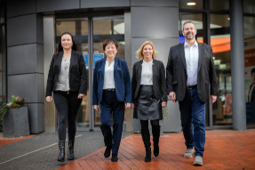 PIA Berater und Beraterinnen der Firma ImmoKonzepte GmbH stehen vor einem grauen Gebäude und lächeln freundlich